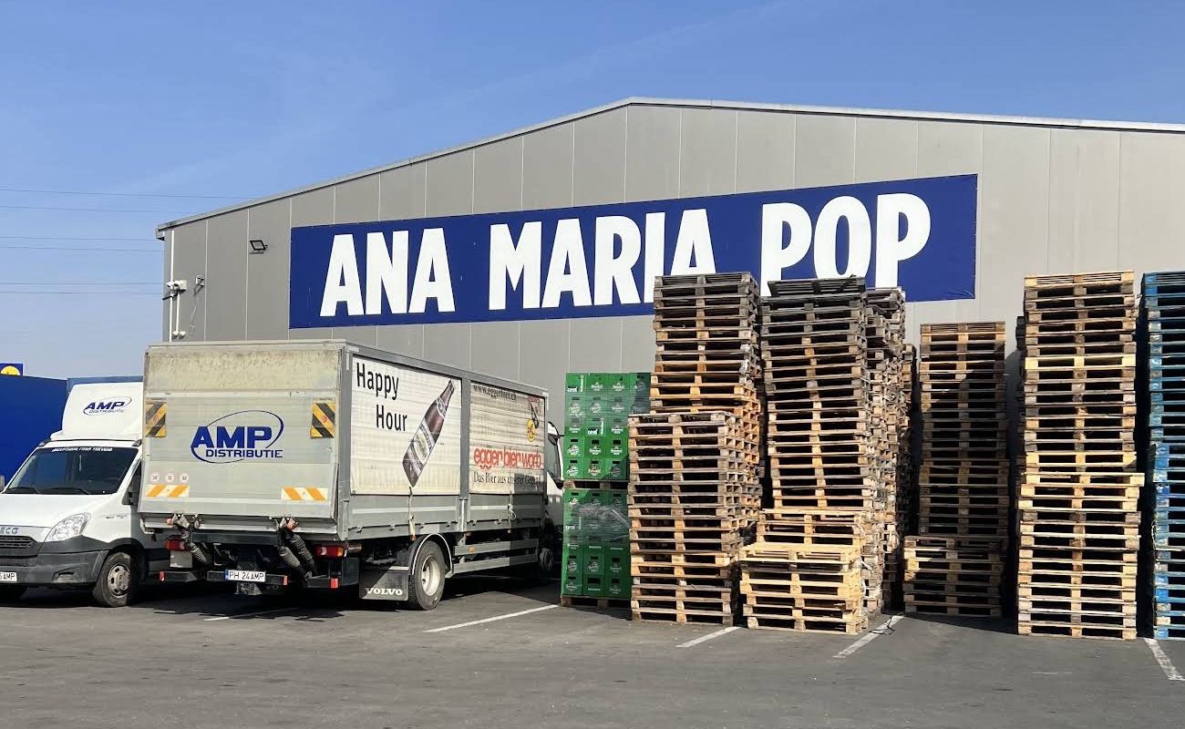 Hala ANA MARIA POP de la Bucov, cu mașini de distribuție AMP și paleți în curte.